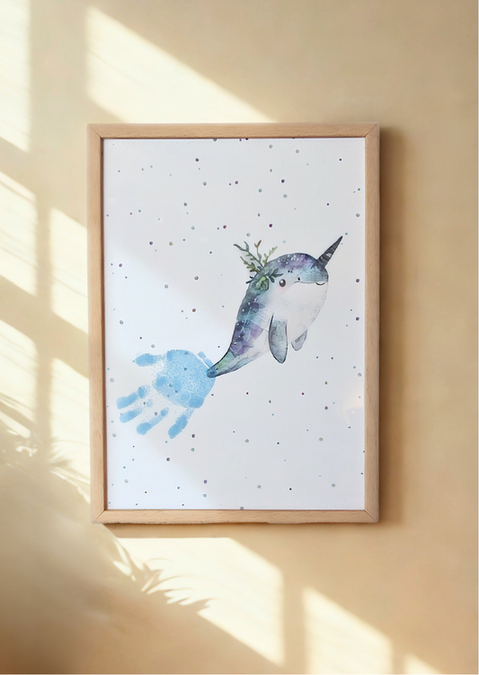 A framed print of narwhal with a child's handprint for its tail