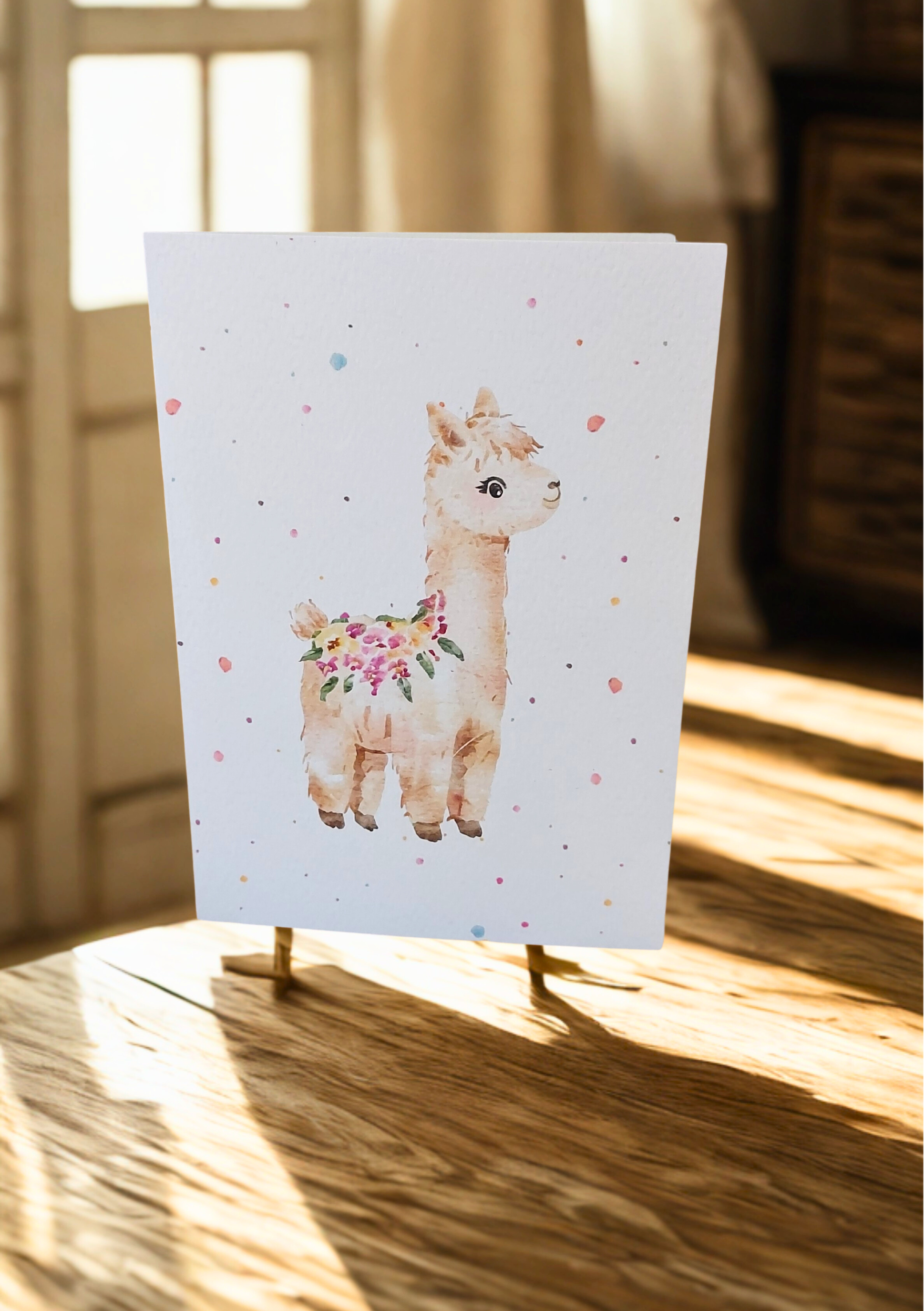 Greetings Card - Watercolour Alpaca. Blank inside. On wooden table with soft sunlight.