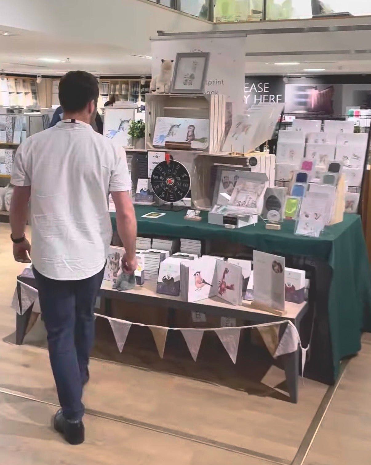 Man walking past a table with books and stationery at an indie pop-up event.