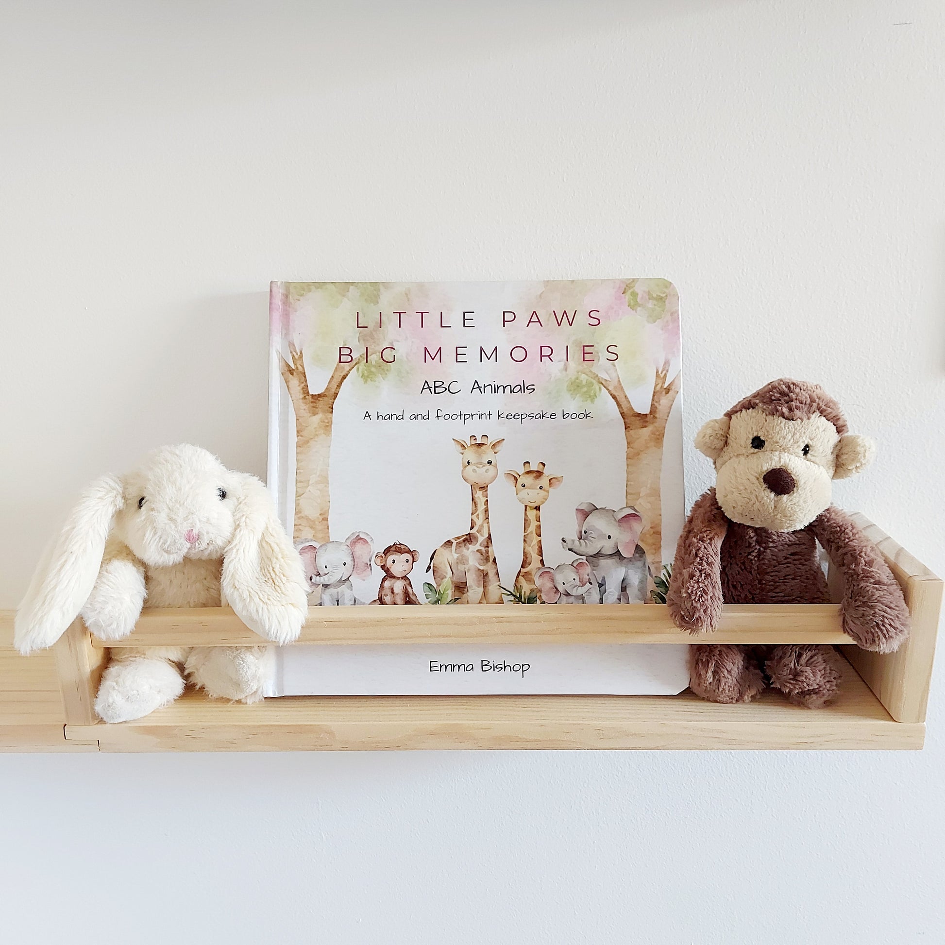 Little Paws Big Memories ABC Animals Baby Hand and Footprint Keepsake Book on a shelf in baby's nursery. Soft toy monkey and rabbit either side of the book. For newborn baby boy or girl, baby shower gift.