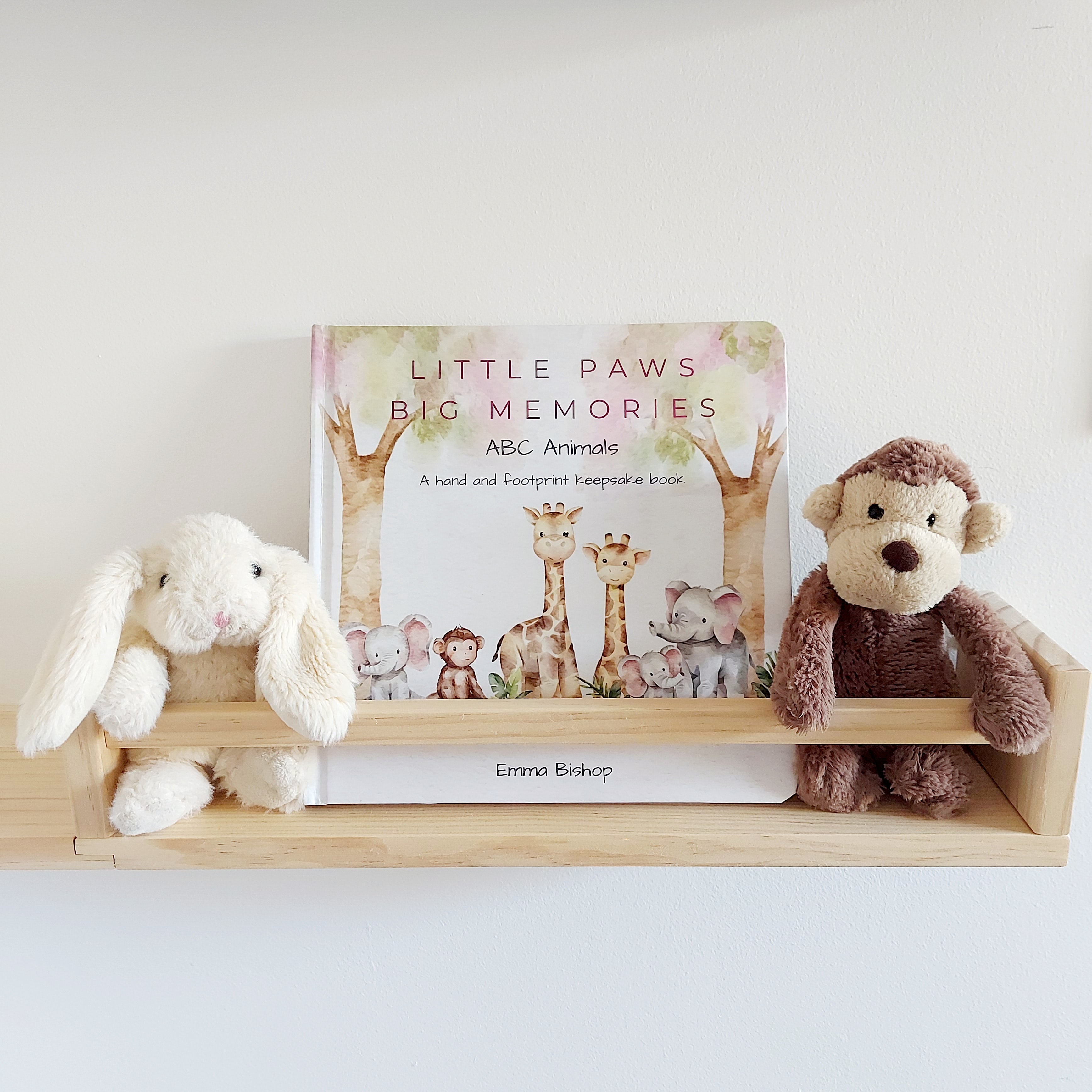 Little Paws Big Memories ABC Animals Baby Hand and Footprint Keepsake Book on a shelf in baby's nursery. Soft toy monkey and rabbit either side of the book. For newborn baby boy or girl, baby shower gift.