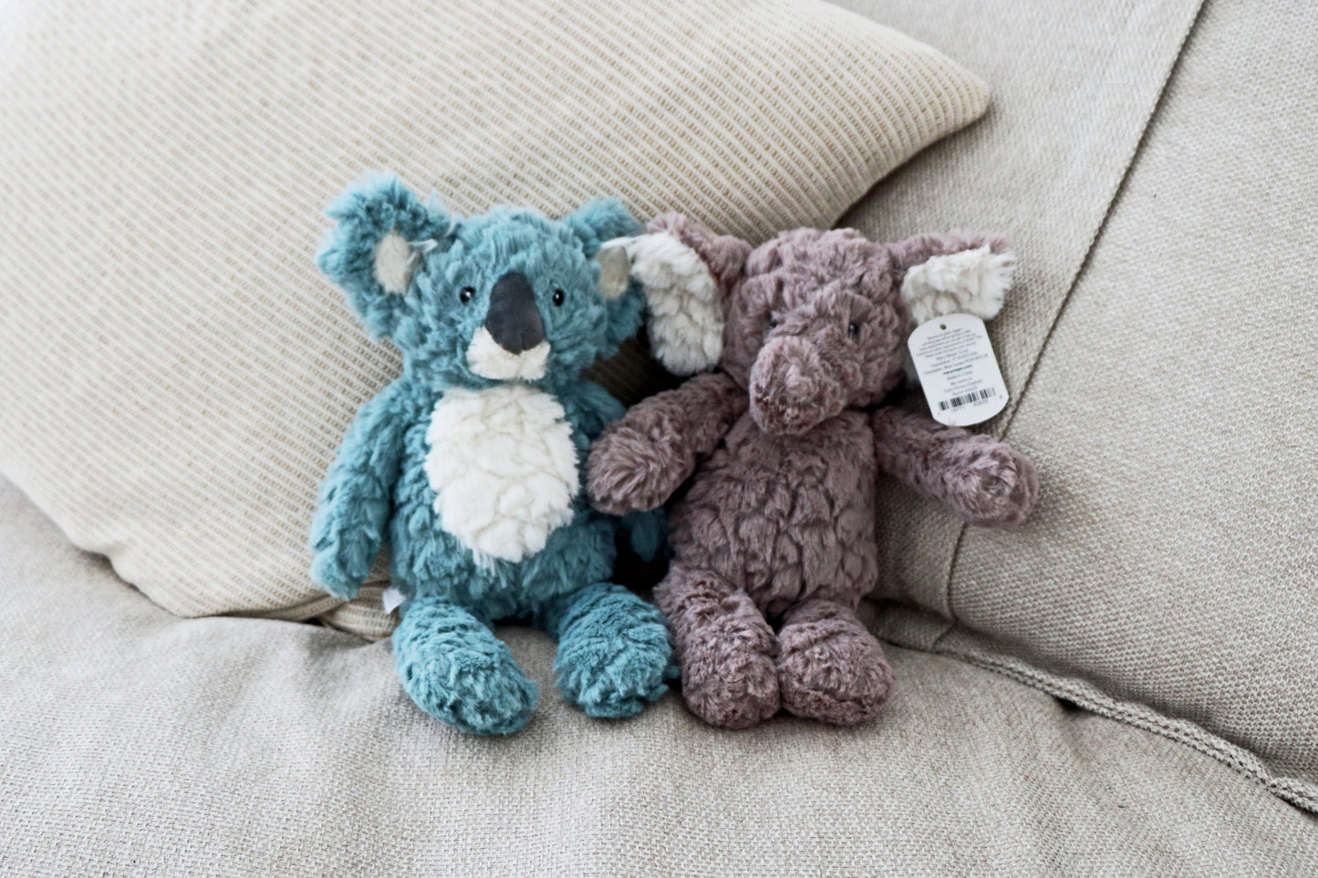 Mary Meyer Putty Elephant and koala soft toy plush for babies and newborn on neutral cushions background. Stuffed animals sitting on sofa side by side together.