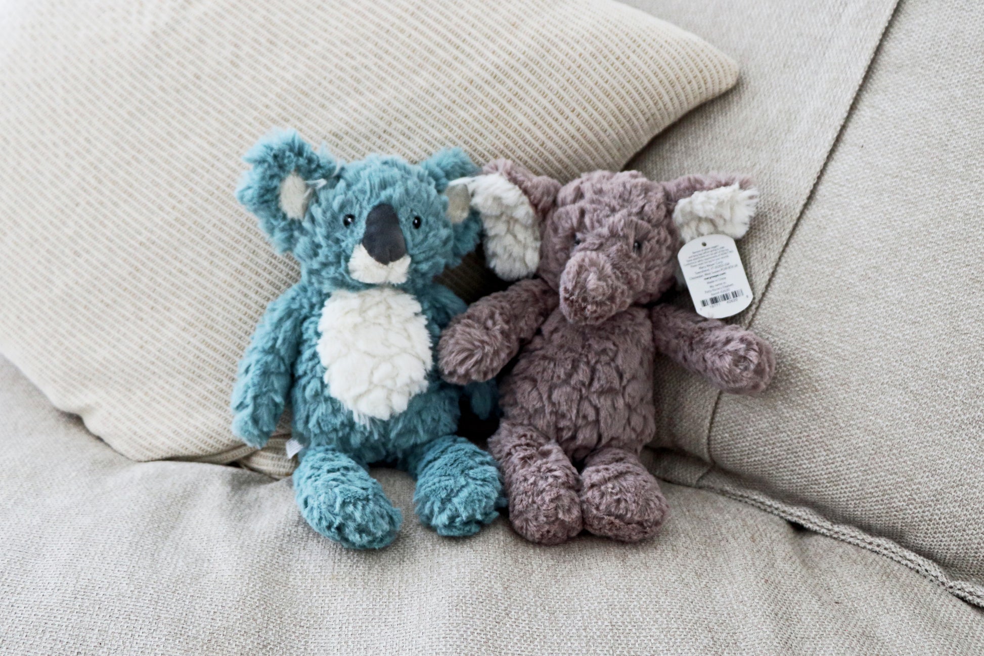 Mary Meyer Putty Elephant and koala soft toy plush for babies and newborn on neutral cushions background. Stuffed animals sitting on sofa side by side together.