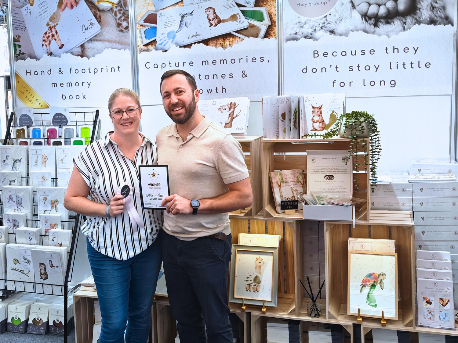 Founders, Emma and Michael holding their award certificate in front of a display of photo books and products.
