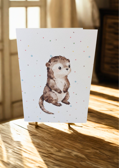 Greetings Card - Watercolour Otter. Blank inside. On wooden table with warm sunlight.