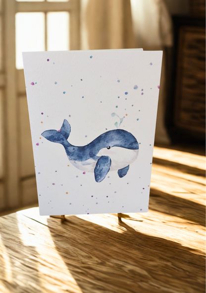 Greetings Card - Watercolour Whale. Blank inside. On wooden table with warm sunlight.